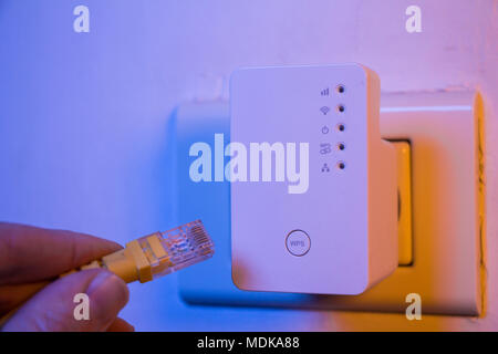 Man insert ethernet cable into WiFi extender device which is in electrical socket on the wall. The device is in access point mode that help to extend  Stock Photo