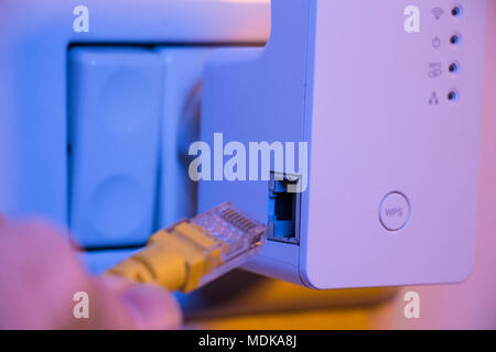 Man insert ethernet cable into WiFi extender device which is in electrical socket on the wall. The device is in access point mode that help to extend  Stock Photo