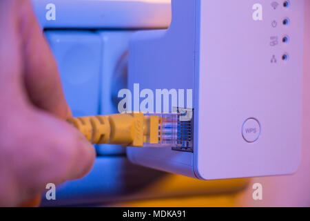 Man insert ethernet cable into WiFi extender device which is in electrical socket on the wall. The device is in access point mode that help to extend  Stock Photo