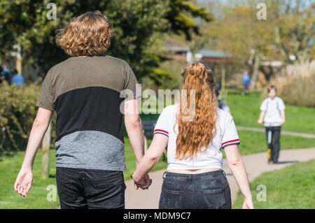 Young couple holding hands talking a Spring walk through a park on a warm Spring day in the UK. Stock Photo