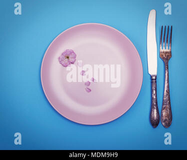 empty round pink ceramic plate and a vintage knife with a fork on a blue surface, top view Stock Photo