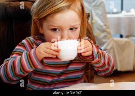A little girl (3 yr old) drinking green tea froma teacup in a chinese restaurant Stock Photo