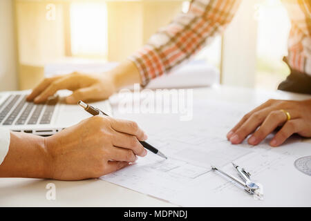 Engineers discuss a blueprint while checking information on a tablet computer in a office. Stock Photo