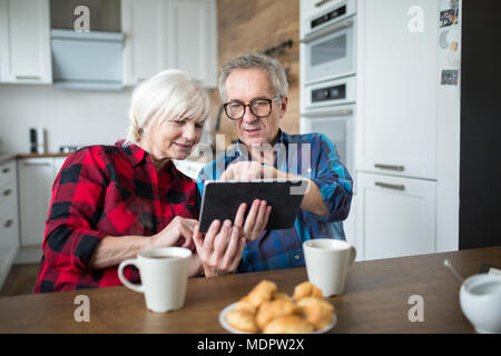 Portrait of senior couple using tablet at kitchen table Stock Photo