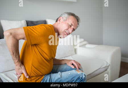 Portrait of senior man suffering from back pain sitting on couch Stock Photo
