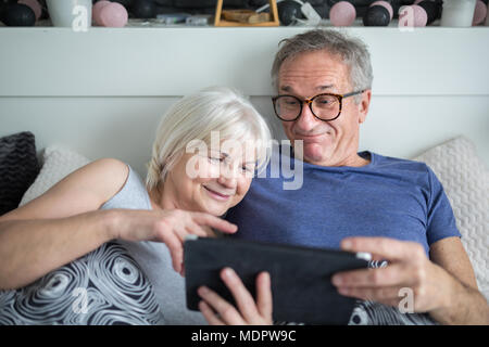 Portrait of happy senior couple lying in bed using tablet Stock Photo