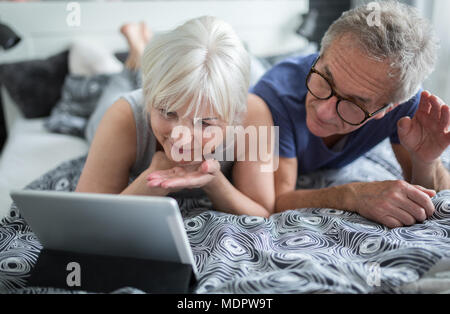 Portrait of senior couple lying on bed having video conversation Stock Photo