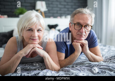 Portrait of senior couple lying on bed propping heads on hands Stock Photo