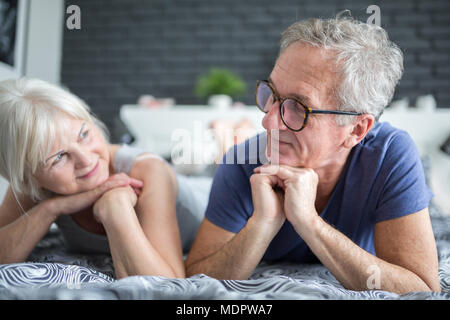 Portrait of senior happy couple lying on bed looking at each other Stock Photo
