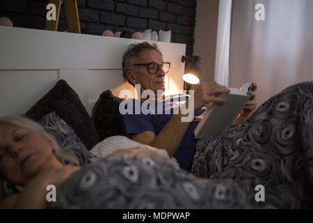 Portrait of senior man lying in bed reading book Stock Photo