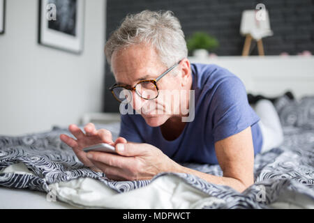 Portrait of senior man lying on bed using smartphone Stock Photo