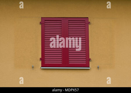 Red wooden shutters on a building with yellow painted walls Stock Photo