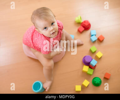 Child sits on chamber pot, toilet, playing with toys. Top view. Stock Photo