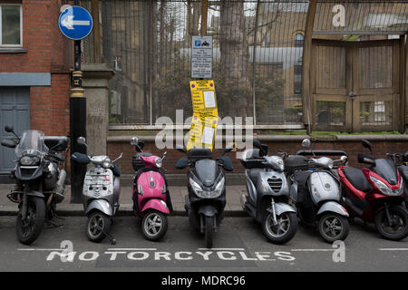 Scooters and motorcycles are left parallel in their specific parking bay with a parking suspension warning sign in Wardour Street, Soho, on 16th April 2018, in London, England. Stock Photo