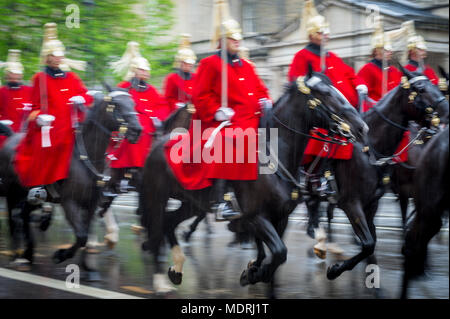 Royal guards on horseback dressed in ceremonial red coats pass with motion blur in a parade on a rainy day in London, England, UK. Shot with slow shut Stock Photo
