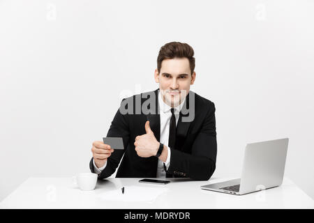 Caucasian office man in formal suit and tie demonstrating digital money in plastic credit card and showing thumb up isolated over gray background. Stock Photo