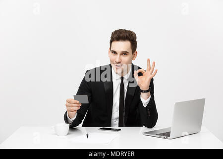 Caucasian office man in formal suit and tie demonstrating digital money in plastic credit card and showing ok isolated over gray background. Stock Photo