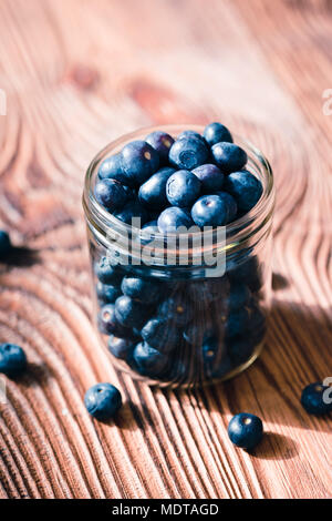 Freshly gathered blueberries put into jar. Some fruits freely scattered on old wooden table Stock Photo