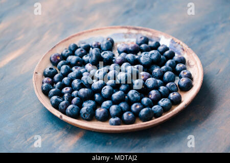 Freshly gathered blueberries put on old ceramic plate. Table painted in blue in the background Stock Photo