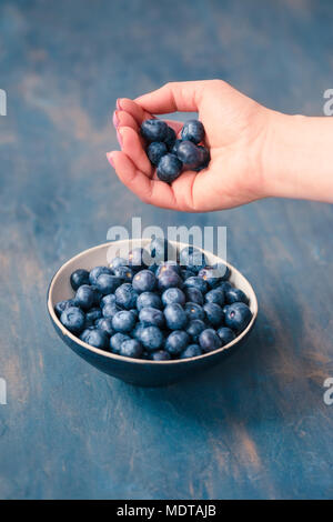 Woman putting freshly gathered blueberries into a small bowl. Table painted in blue in the background Stock Photo