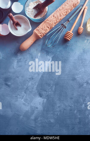 Baking tools and ingredients from above. Rolling pin, honey spoons, a whisk, measuring spoons, flour, sugar, and egg shells on a concrete background with copy space. Minimalist cooking concept Stock Photo