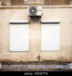 Old yellow wall with two windows and air conditioner Stock Photo