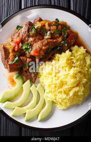 Seco de chivo is goat stew with yellow rice and fresh avocado close-up on a plate. Vertical top view from above Stock Photo