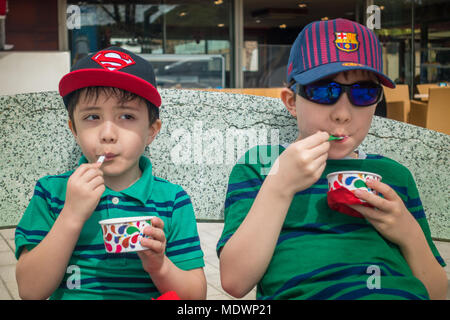 Young boys sit together eating tubs of ice cream Stock Photo