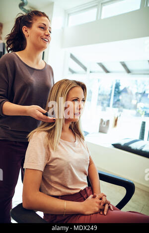 Young blonde woman sitting in a chair discussing her hair with her hairstylist during a salon appointment Stock Photo