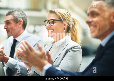 Smiling mature businesswoman clapping hands with two male coworkers while sitting at a table during an office presentation Stock Photo