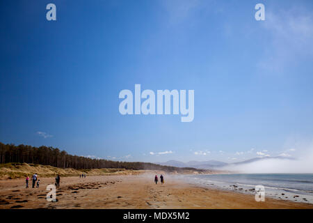 North Wales, UK 20th April 2018, UK Weather:  A high weather front will remain over the UK for the coming days and into the weekend people begin to head to the beach with visitors heading to Newborough Warren and beach on Anglesey in the warm weather and sea mist and the Snowdonia National Park in the distance © DGDImages/Alamy Live News Stock Photo