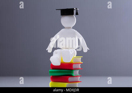 Human Figure With Graduation Hat Sitting On Multi Colored Stacked Books Stock Photo