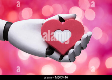 Robot Holding Red And White Heart On Pink Background Stock Photo