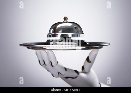 Robotic Hand Holding Service Bell In Plate Against Grey Background Stock Photo