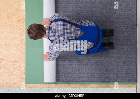 Side View Of A Young Male Worker In Overalls Installing Carpet Stock Photo