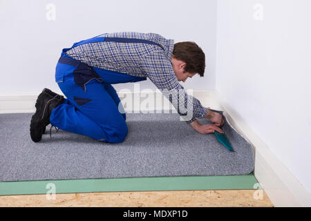 Side View Of A Male Worker Fitting Grey Carpet On Floor Stock Photo
