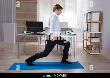 Side View Of A Young Businessman Doing Stretching Exercise On Exercise Mat In Office Stock Photo