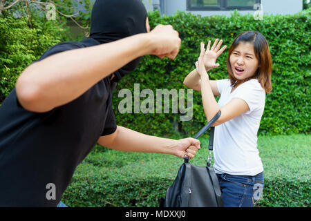 Thief fighting and stealing handbag from screaming asian woman at park Stock Photo