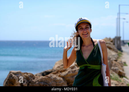 Young woman in a green dress with a ship captain hat on a pier Stock Photo