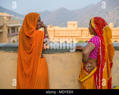 Two women in colourful traditional Indian clothing stand talking and looking out in Amer Fort; Jaipur, Rajasthan, India Stock Photo