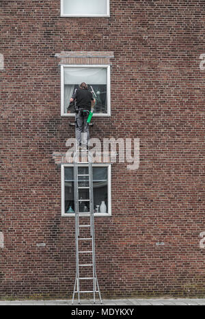 window cleaner is high on a ladder to wash a window of an apartment building Stock Photo