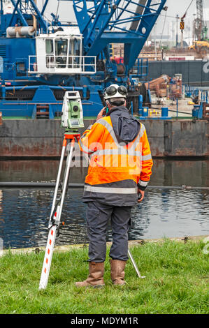 construction worker standing on a lawn near a digital land surveyor calling with his mobile phone Stock Photo