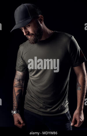 Pensive Black bearded male dressed in a grey shirt, sunglasses and baseball cap. Stock Photo