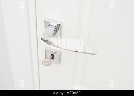 Modern glossy chrome door handle and keyhole with key. Close-up elements of the interior of the apartment. White door and white wall Stock Photo