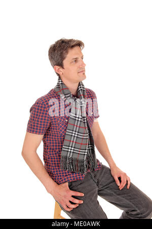 A handsome young man in a checkered shirt and scarf around he neck sitting relaxed, isolated for white background Stock Photo