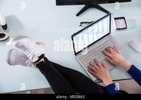 Businessperson's Hand Working On Gantt Chart Using Laptop With Crossed Legs On Office Desk Stock Photo