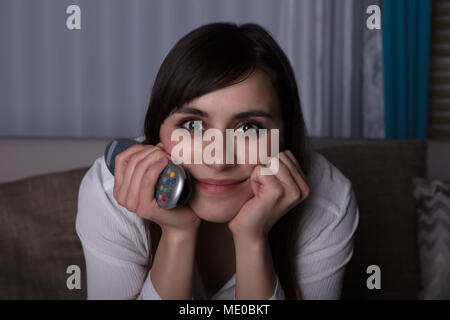 Portrait Of A Contemplated Young Woman Holding Television Remote Control Stock Photo
