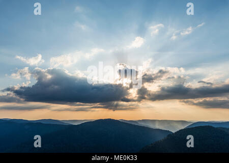 Overview of the silhouetted Vosges Mountains at sunset with sun breaking though the clouds at Le Markstein in Haut-Rhin, France Stock Photo