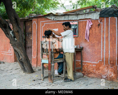 A man shaving another man's face with a set up of table and chair along the street; Jaipur, Rajasthan, India Stock Photo