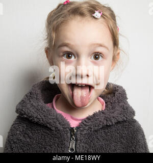 Cute little girl showing tongue out in big sun hat sitting on road